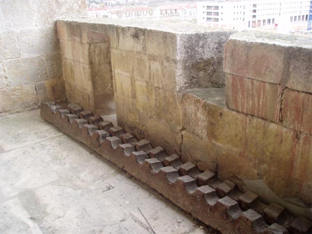 Muralla de la Iglesia de San Juan con sus almenas y saeteras, el artilugio de madera se usaba para atar de pies y manos a los presos en la Edad Media